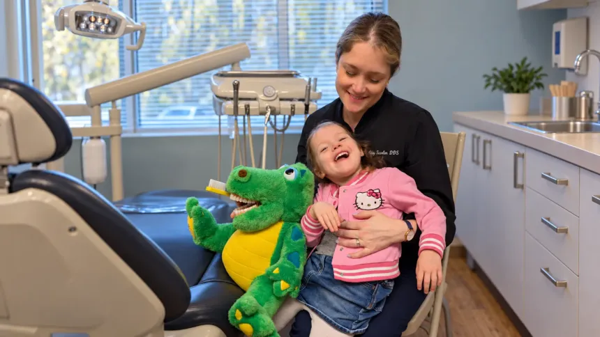 Dr. Abigail Scanlan sharing a joyful moment with her daughter Chloe and Toothy the Dinosaur in the dental office