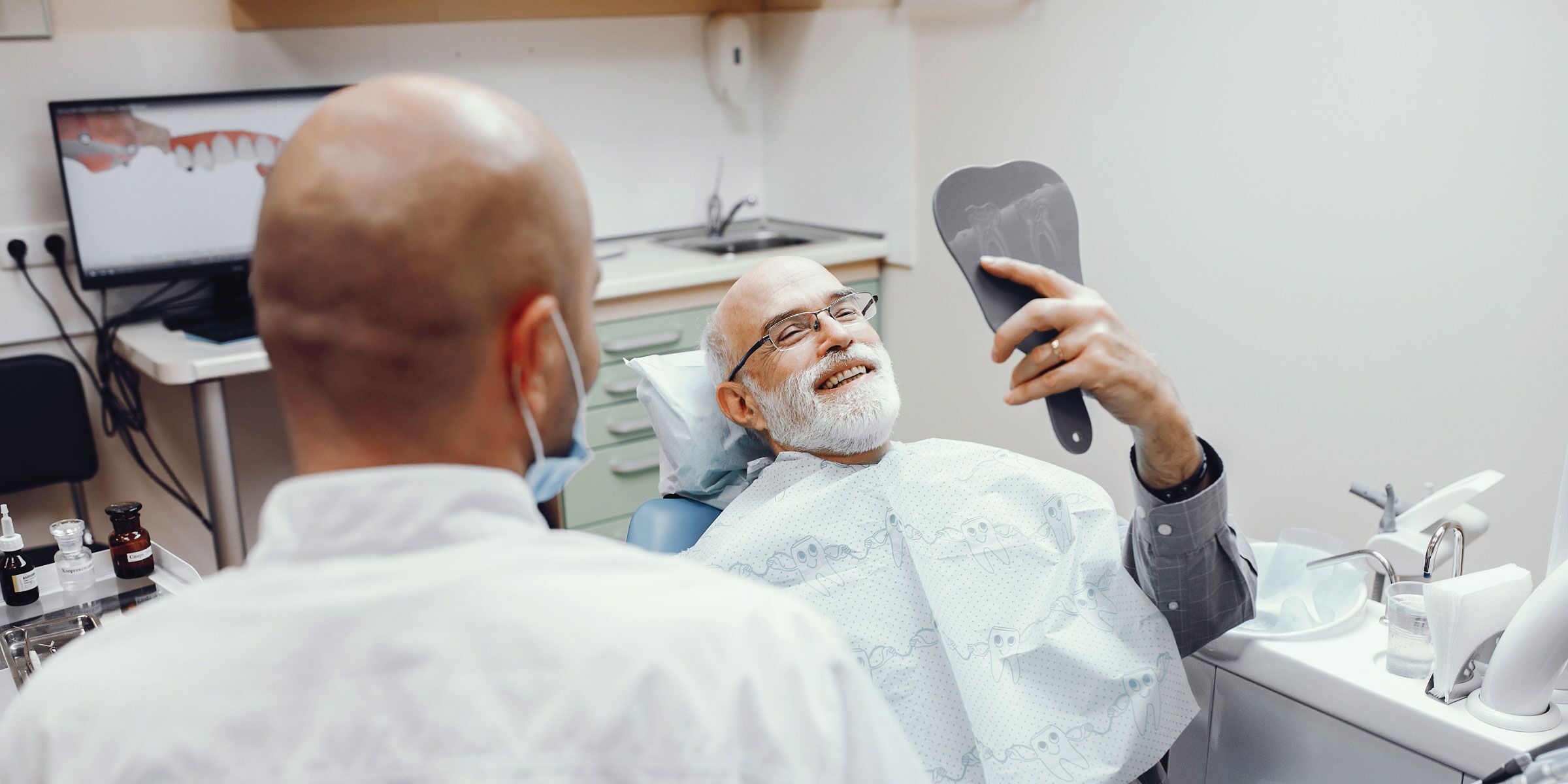 An older patient viewing his smile in a hand mirror during a denture consultation